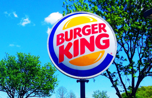 A burger King sign amongst the trees and clear sky.