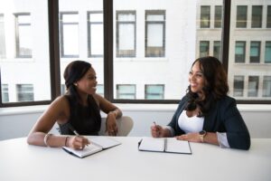 Two woman in business attire sit at a table for an interview.