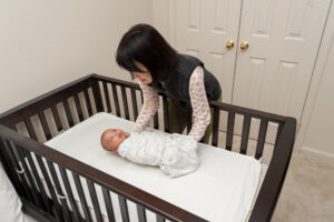 A mother gently places her baby in a crib.