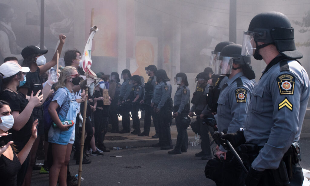 A group of protestors stands across from a row of police officers in riot gear.