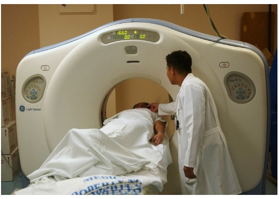 Picture of a patient laying on a table that moves through the middle of the CT scanner.