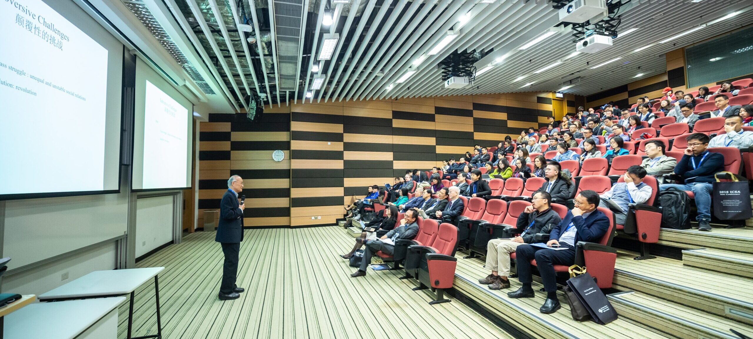 Man speaking in front of a slideshow to an audience sitting in a lecture hall