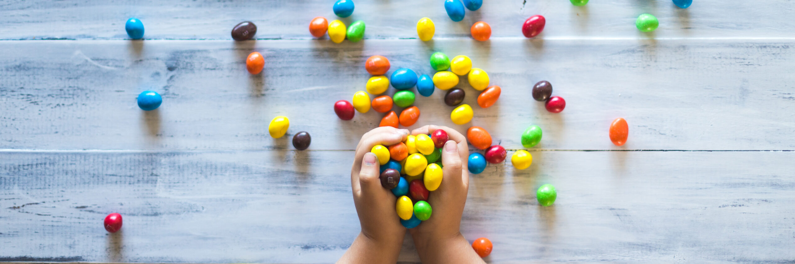 Photo of a child holding different colored candies on gray wooden pallet board.